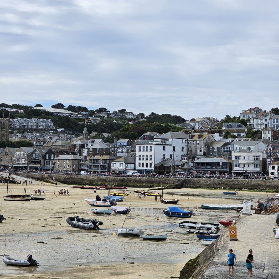 Unlocking Your 2024 Travel Adventure: Tips for Planning Ahead A coastal town perfect for travel adventure, with boats resting on the sandy shore at low tide, rows of houses behind, and people strolling along the waterfront beneath a cloudy sky.