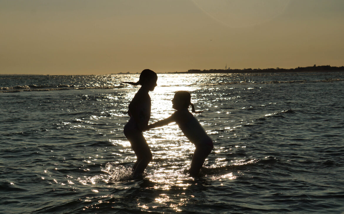 Tide and Time: Essential Tips for Your Next Seaside Adventure Two children are silhouetted against the setting sun as they play in shallow sea water, creating splashes and reflections—capturing the joy found by following essential tips for seaside adventures.