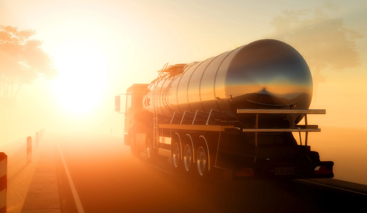 A shiny diesel lorry tanker drives down a foggy road at sunrise, bathed in warm, golden light, with trees faintly visible in the background—ready for long road journeys ahead.