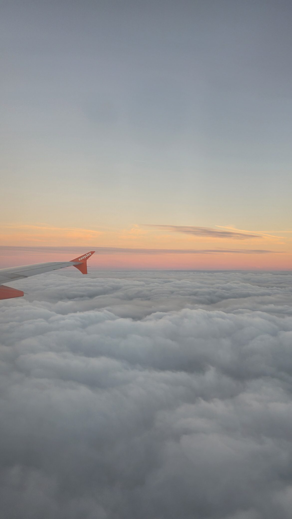 Barrierless Airport Parking in 2026: How ANPR Works and What UK Travellers Need to Know View from an aeroplane window over a thick layer of clouds during a pastel sunset, with an orange easyJet wingtip visible, contrasting with the efficient ANPR technology used at modern UK airport car parks.